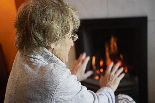 An elderly lady warms her hands in front of the fire