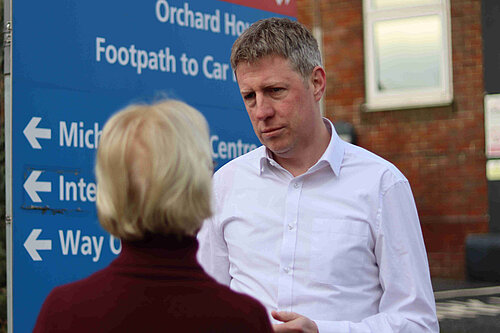 James MacCleary talking to a constituent next to an NHS signboard