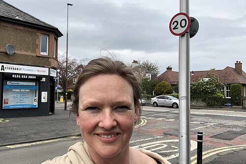 Sanne standing in front of a 20 miles per hour sign at a road junction.