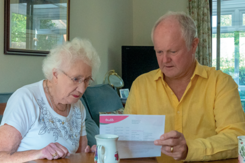 Clive Jones MP sat down with an elderly woman in a sitting room, both of whom are reading a piece of paper with a concerned look on their face.