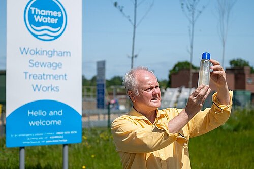 Clive Jones stood outside of Thames Water Wokingham Sewage Treatment Works holding a transparent container filled with contaminated river water.