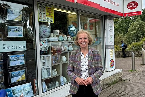 Susan Murray, MP for Mid Dunbartonshire, standing smiling in front of a post office.