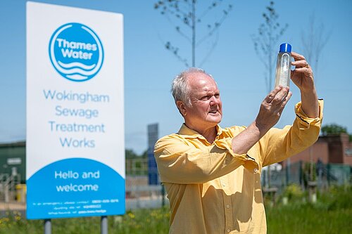 Clive Jones inspecting a glass bottle containing dirty river water outside of Thames Valley's Sewage Treatment Works