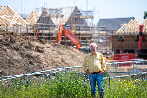 Clive Jones stood in front of a building site. Half-built houses and construction equipment can be seen in the background.