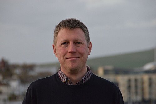 James MacCleary head and shoulders against blurred background of buildings and sky